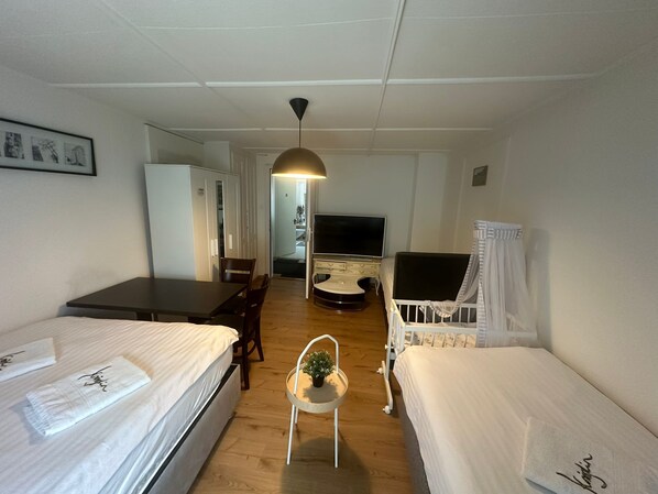 A hotel room with two beds, a dining table, a TV, and a small plant.