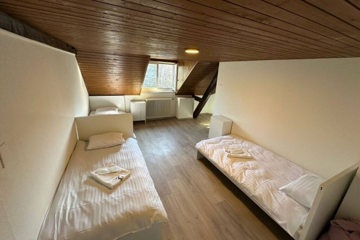 A small, cozy attic bedroom with two single beds, a window, and a sloped ceiling.