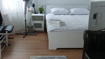A bedroom with a bed, a bedside table with a lamp, a small plant, and a colorful painting on the wall.