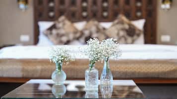 A bedroom with a bed, pillows, and two glass vases with flowers on a glass table.