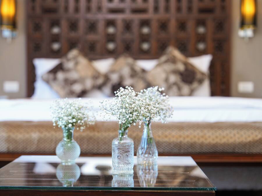 A bedroom with a bed, pillows, and two glass vases with flowers on a glass table.