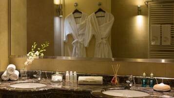 A hotel bathroom with two sinks, a large mirror, and a towel rack with robes.