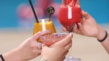 A close-up of hands holding cocktail glasses with straws and garnishes.