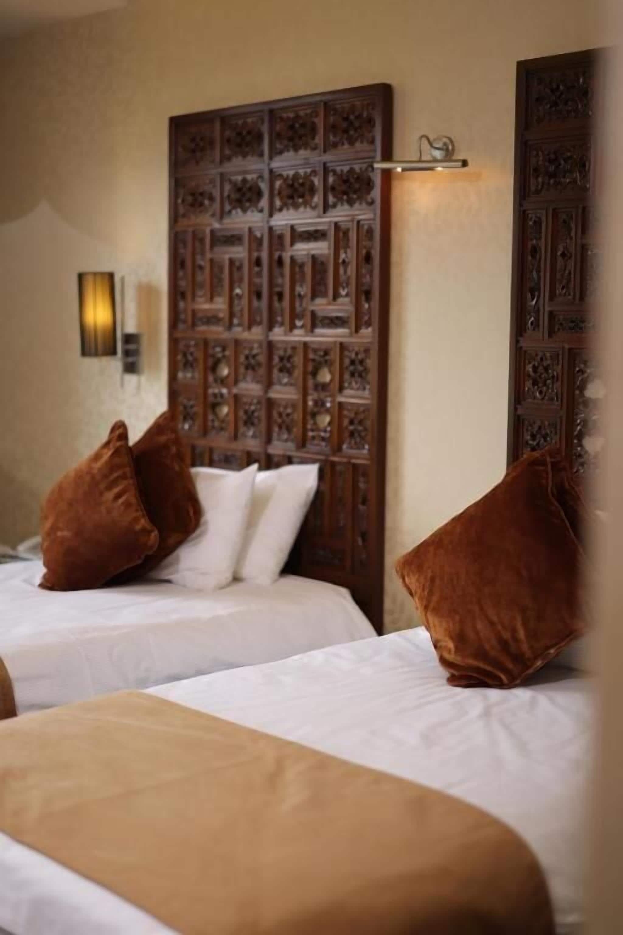 Een hotelkamer met twee bedden, een decoratief houten hoofdeinde en een wandlamp.