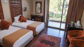 Habitación de hotel con dos camas, un balcón con vistas, cabecera de madera, una mesita con un florero y una alfombra estampada.