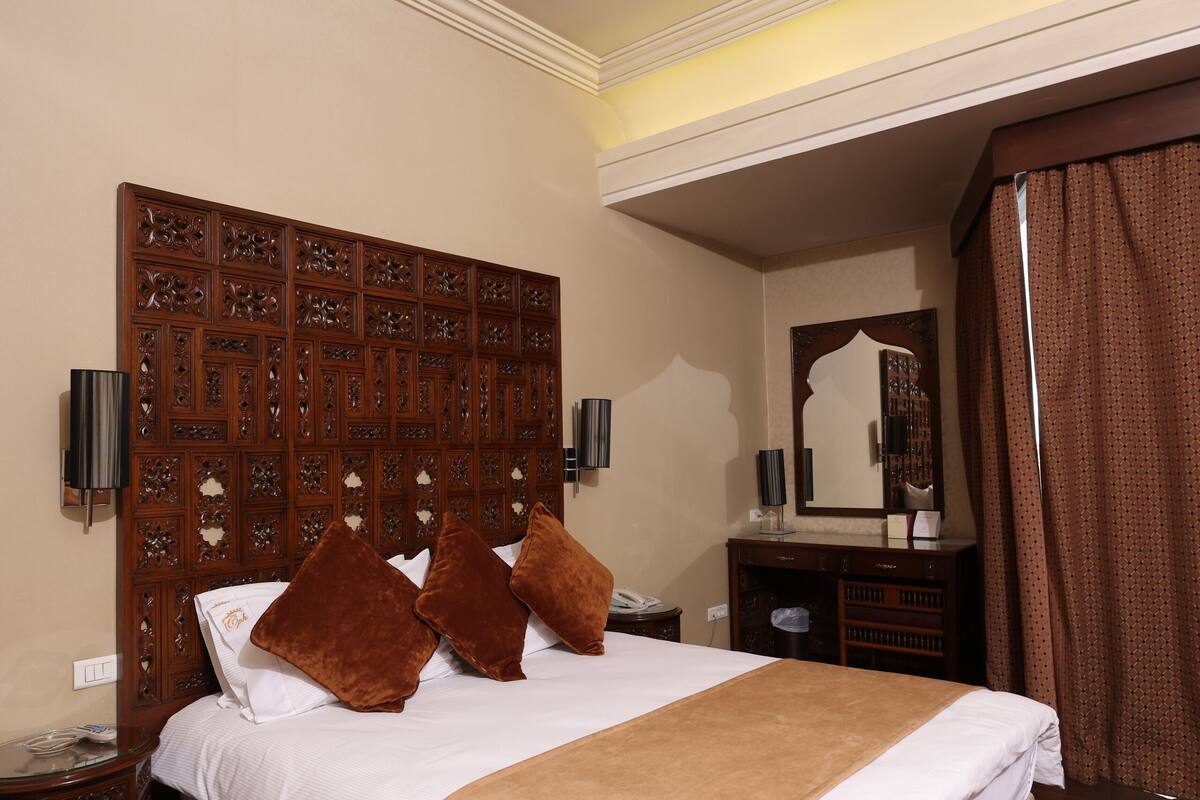 A hotel room with a large bed, wooden headboard, and a mirror above the dresser.