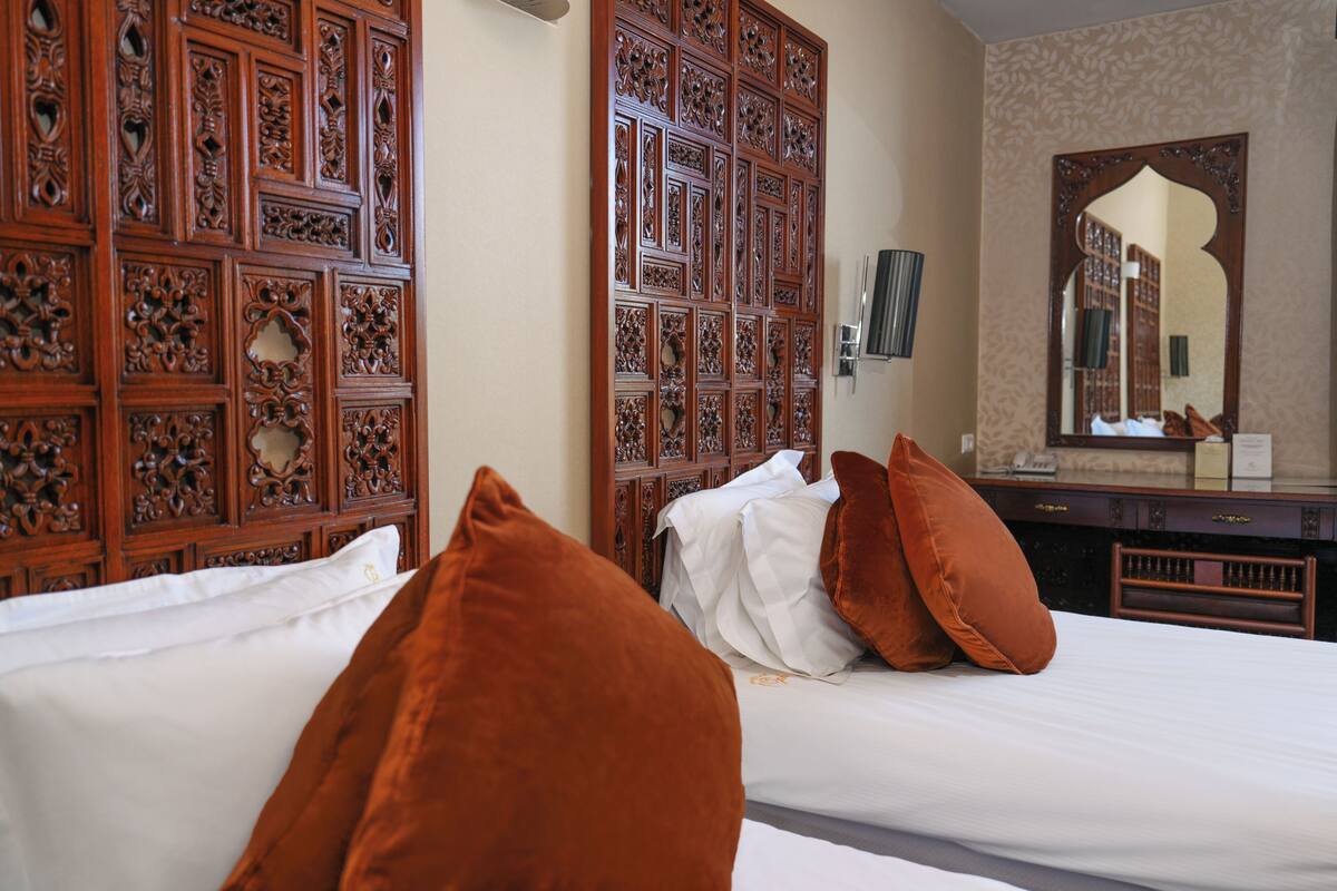 A hotel room with a large wooden panel wall, a bed with white and brown pillows, a dresser, and a mirror.