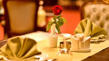 A dining table set with a rose in a vase, a green napkin, and a silver bowl.