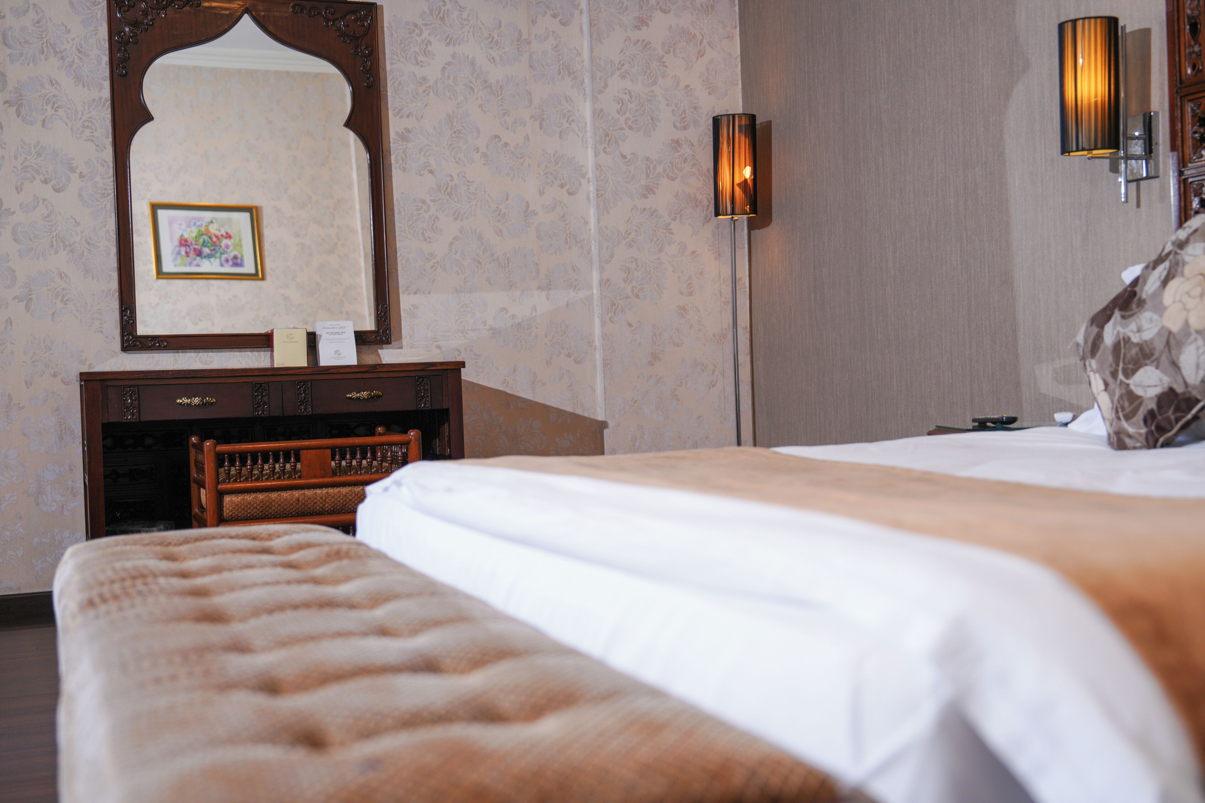 A hotel room with a large bed, a wooden dresser, a mirror, and a wall-mounted lamp.