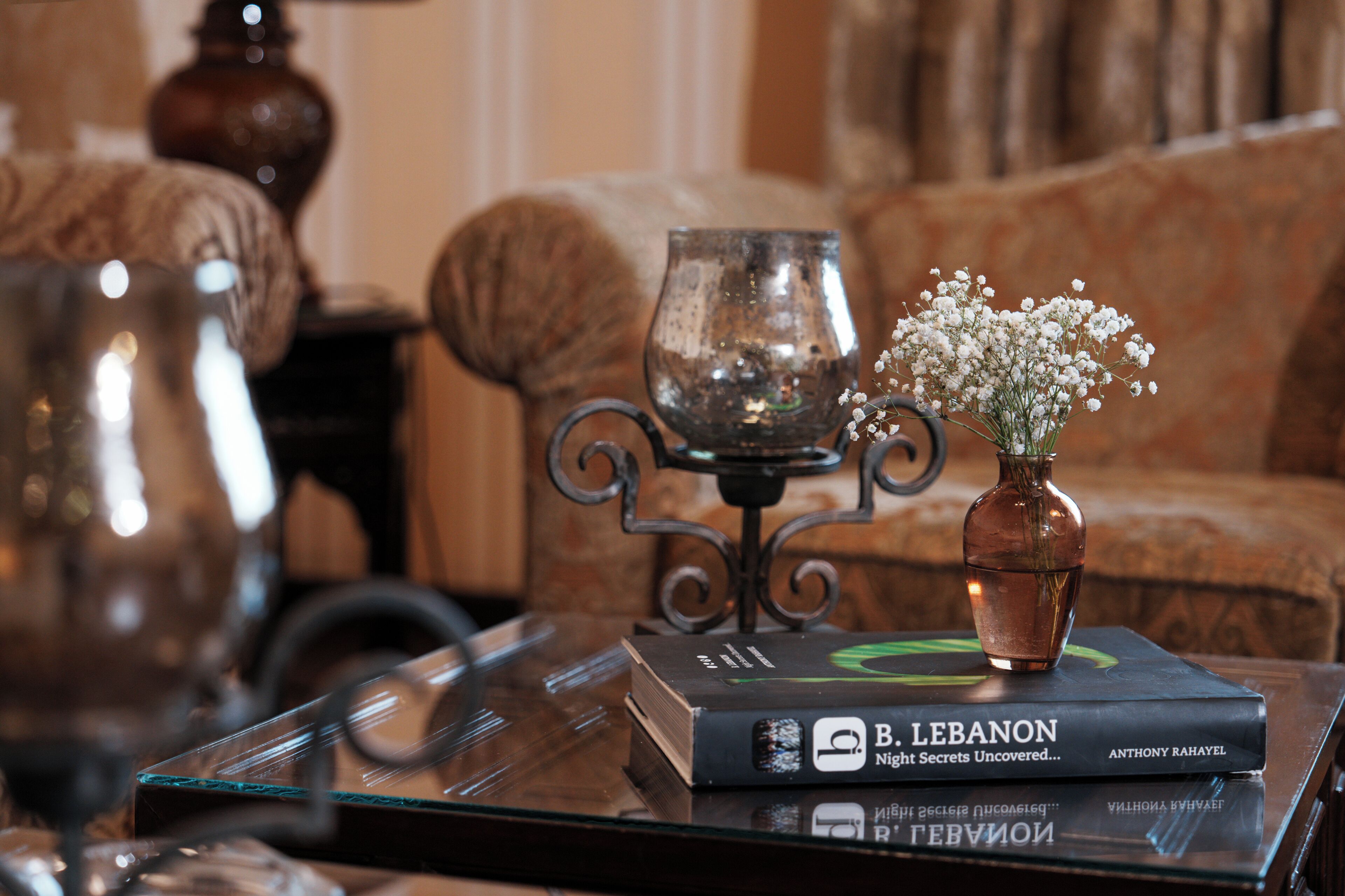 A book titled 'B. Lebanon' on a glass table with a vase of flowers and a candle holder.
