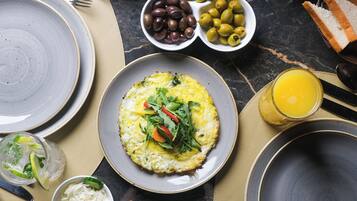 A breakfast setting with plates of food, olives, olives, and a glass of orange juice.