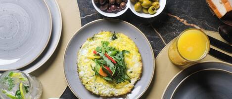 A breakfast setting with plates of food, olives, olives, and a glass of orange juice.