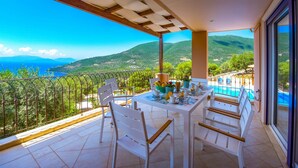 A balcony with a table set for dining, overlooking a mountainous landscape and a body of water. - Villa Andromeda-Pegasus (Sivota)