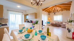 A spacious living area with a dining table set for four, a kitchen in the background, and a cozy seating area with a sofa and armchairs. - Villa Andromeda-Pegasus (Sivota)