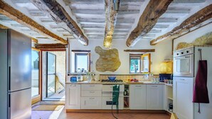 Eine Küche mit weißen Schränken, einer Wand mit Natursteinoptik, einem Gasherd und einer Mikrowelle.