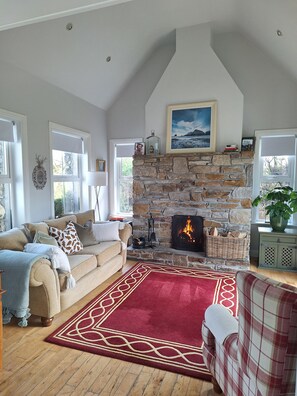 A cozy living room with a stone fireplace, a sofa, a red rug, and a view of the outdoors.
