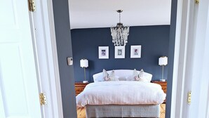 A bedroom with a wooden floor, a bed with white bedding, a chandelier, and framed pictures on the wall.