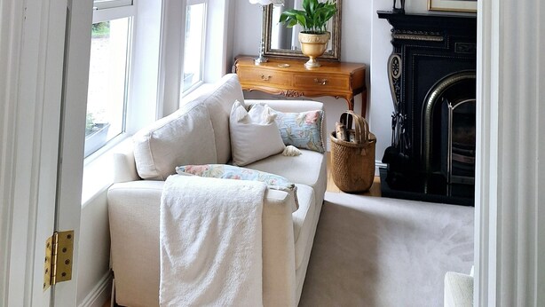 A room with a white sofa, a mirror, a fireplace, and a window.