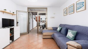 A modern living room with a sofa, TV, and a dining area visible through an open door.