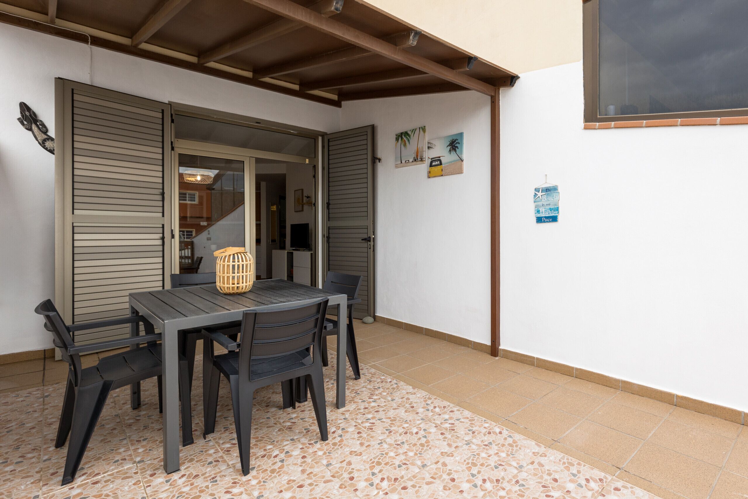 A covered patio with a table and chairs, a woven basket, and a tiled floor.