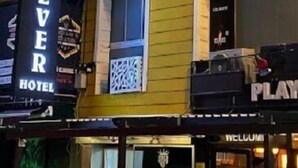 Un hotel con un evidente cartello 'SEVER HOTEL', un balcone caratterizzato da un'elaborata lavorazione a reticolo e un cartello 'WELCOME' visibile sullo sfondo.