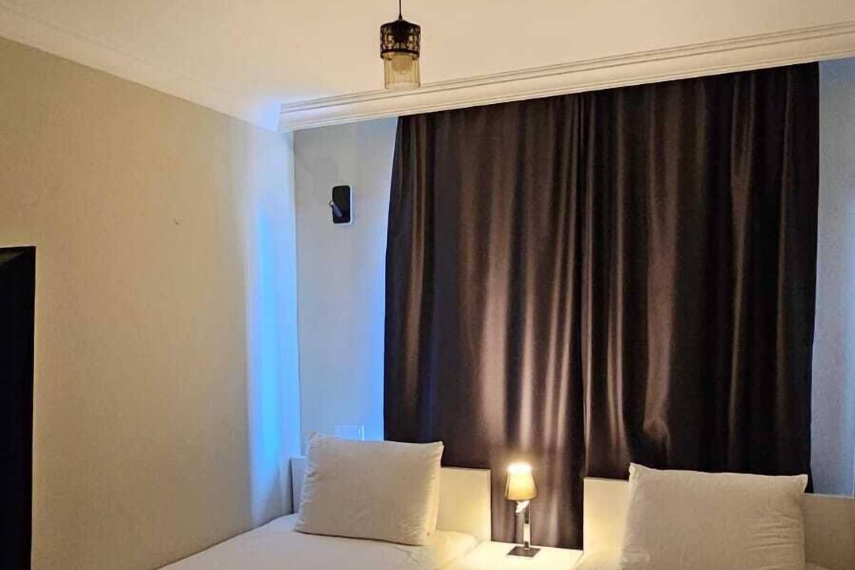Una habitación de hotel con dos camas individuales, un ventilador de techo, una lámpara de noche y una cortina oscura.
