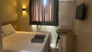 A hotel room with a bed, a desk, a chair, a TV, and a window with curtains.