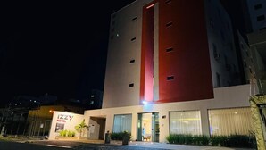 Een hotel met een moderne gevel, een opvallend rood accent en een goed verlichte ingang.