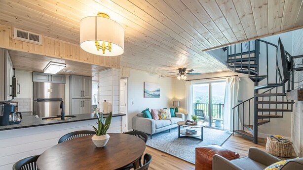A modern interior with a wooden ceiling, a dining area, a kitchen, a living room with a sofa and coffee table, and a staircase.