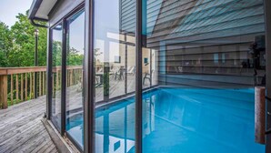 A swimming pool with glass walls, a wooden deck, and a view of the surrounding greenery. - Two Bed Room Condo Mountain Views Indoor Pool (Gatlinburg)