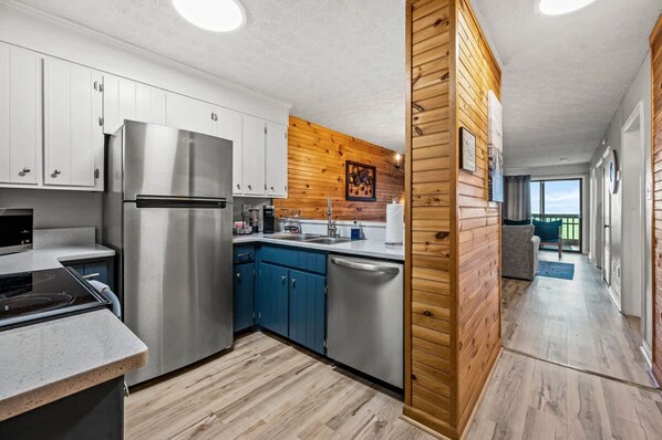 A modern kitchen with stainless steel appliances, blue cabinets, and a wooden accent wall.