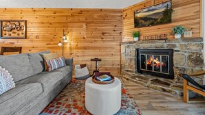 A cozy living room with a stone fireplace, a gray sofa, and a wooden wall. - Two Bed Room Condo Mountain Views Indoor Pool (Gatlinburg)