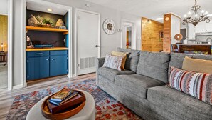 A modern living room with a grey sofa, a wooden cabinet, and a kitchen area visible through an open door. - Two Bed Room Condo Mountain Views Indoor Pool (Gatlinburg)