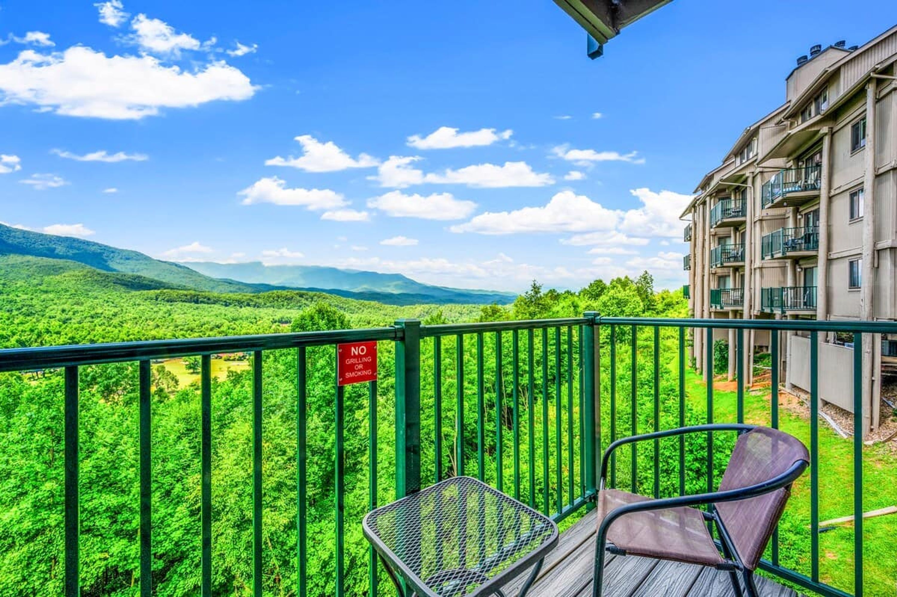 A balcony with a view of a lush green landscape and a building with balconies.