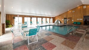 An indoor swimming pool with lounge chairs and a small table, surrounded by wooden paneling and large windows. - Loft Sleeps 8 Views Indoor Pool Access (Gatlinburg)