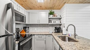 A modern kitchen with grey cabinets, stainless steel appliances, a granite countertop, and a wooden ceiling. - Loft Sleeps 8 Views Indoor Pool Access (Gatlinburg)