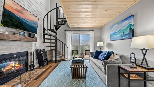A modern living room with a fireplace, a spiral staircase, a sofa, and a large painting. - Loft Sleeps 8 Views Indoor Pool Access (Gatlinburg)