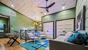 Un'accogliente stanza con soffitto in legno, una ventola a soffitto, un tavolo da calcio, un divano con cuscini decorati e un'ampia finestra con vista.