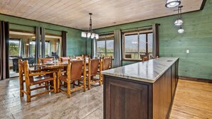 Un'ampia sala da pranzo con tavolo e sedie in legno, un'isola centrale e ampie finestre che offrono vista all'esterno.
