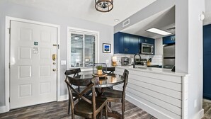 Una cocina moderna con armarios blancos, una isla central y un comedor con una mesa redonda y sillas de madera.