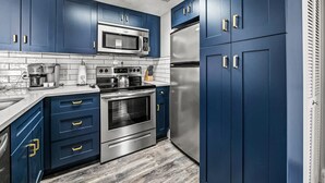 Una cocina moderna con gabinetes azules, electrodomésticos de acero inoxidable y salpicadero de azulejos.