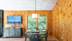 A wooden-paneled room with a dining table, chairs, a television, and a window with a view of trees.