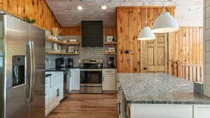 A kitchen with wooden walls, a stainless steel refrigerator, an oven, and a marble countertop.