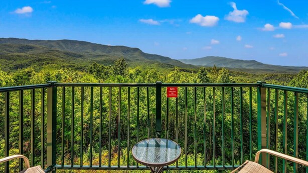 A balcony with a glass table and chairs, overlooking a forested landscape with mountains in the distance. - Sleeps 4 Mountains Views Indoor Pool Sauna (Gatlinburg)