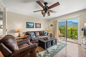 A spacious living room with a leather sofa, a coffee table, and a ceiling fan. There is a balcony with a view of the mountains. - Sleeps 4 Mountains Views Indoor Pool Sauna (Gatlinburg)
