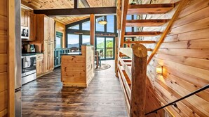 A wooden cabin interior with a kitchen, dining area, and large windows offering a view of the outdoors. - 180 Views Sleeps 7 Private Hot Tub Full Kitchen (Gatlinburg)