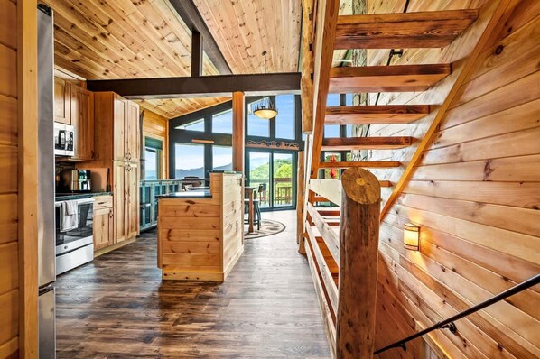L’intérieur d’un chalet en bois comprend une cuisine, un coin repas et de grandes fenêtres qui offrent une vue sur l’extérieur.