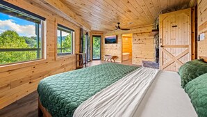 A wooden cabin bedroom with a large bed, a ceiling fan, and a view of the forest. - 180 Views Sleeps 7 Private Hot Tub Full Kitchen (Gatlinburg)