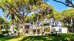A modern house with a white exterior, surrounded by lush greenery and trees. - Spectacular Villa in Quinta do Lago - Private Pool, BBQ & 5-Star Concierge (Faro)