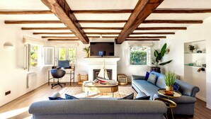 A modern living room with exposed wooden beams, a fireplace, a blue sofa, and a small sailboat model. - Spectacular Villa in Quinta do Lago - Private Pool, BBQ & 5-Star Concierge (Faro)